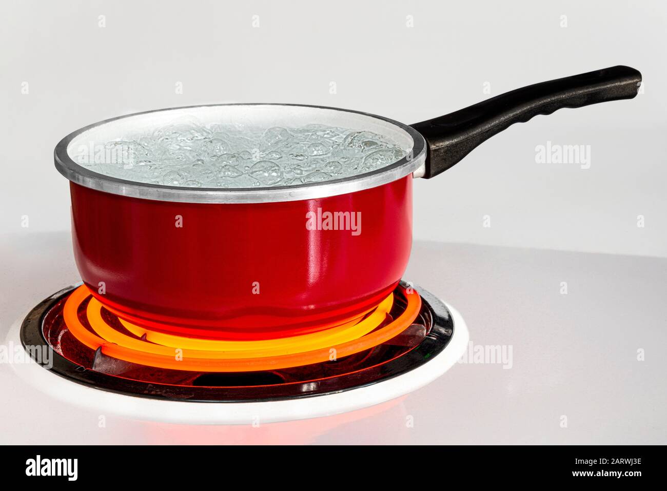 Colpo orizzontale di una pentola rossa di acqua bollente su una stufa con il bruciatore girato ad alto. Foto Stock