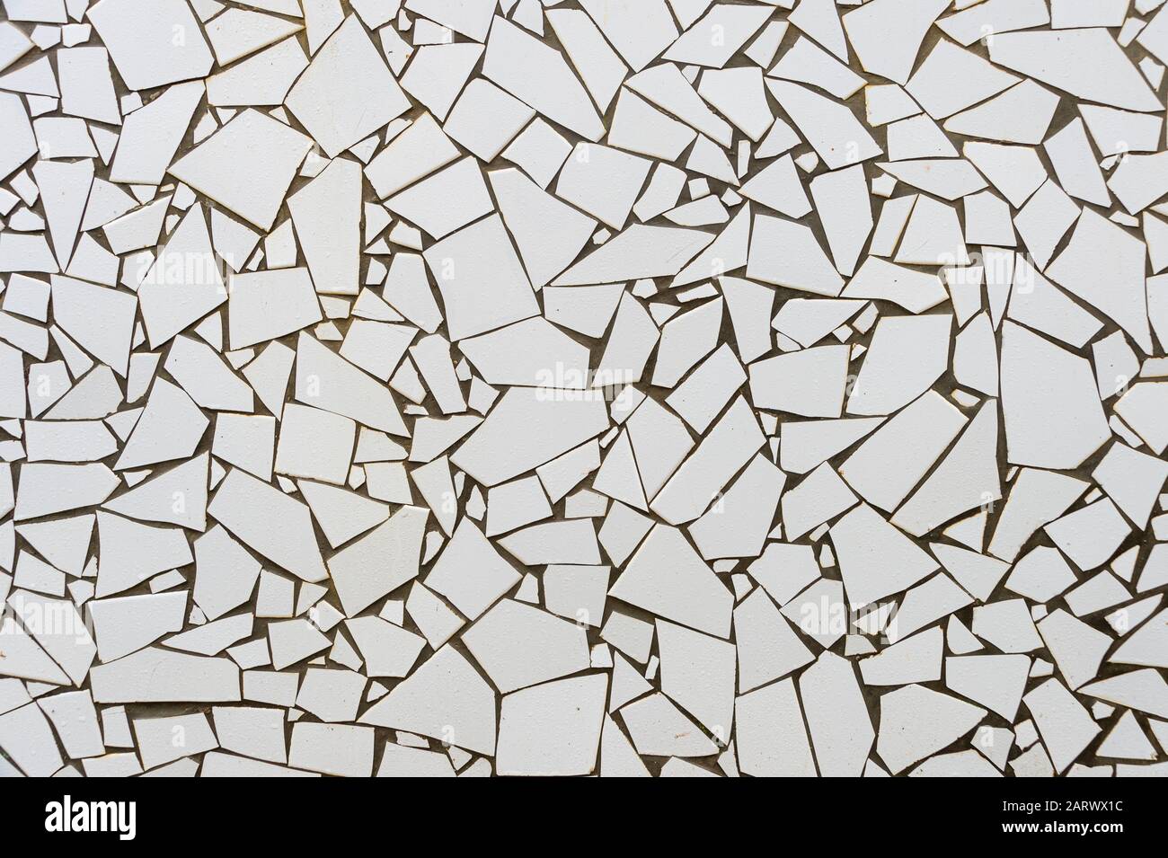le piastrelle bianche rotte si sono inserite in cemento su una parete per creare un motivo e una texture interessanti. Foto Stock