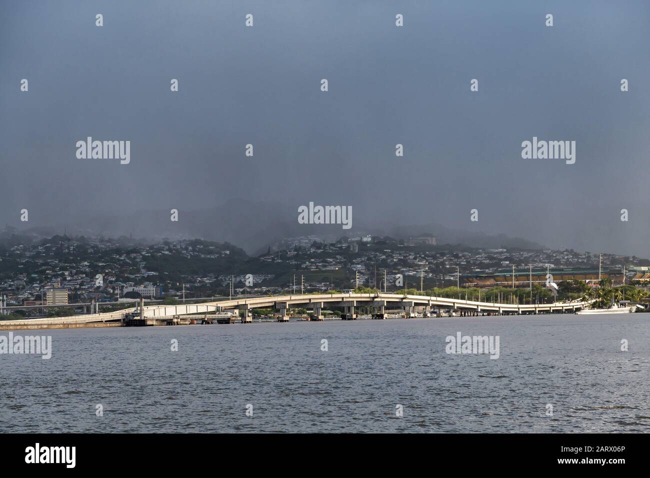 Oahu, Hawaii, Stati Uniti. - 10 Gennaio 2020: Pearl Harbor. Il ponte di Ford Island fruma la linea bianca tra l'acqua grigia una cintura di verdi colline con case bianche. A. Foto Stock