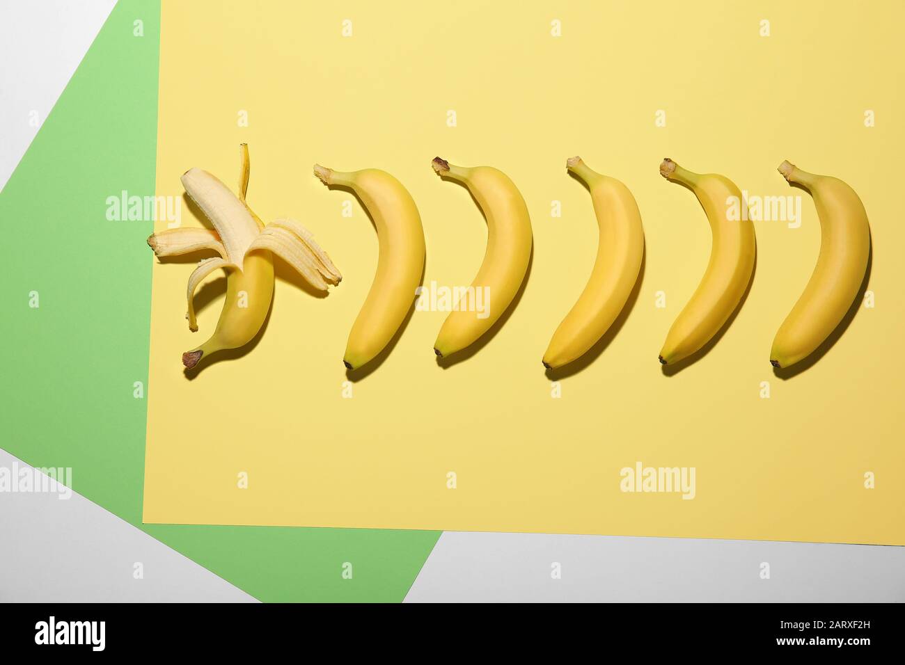 Banana sbucciata tra quelli non sbucciati su sfondo colorato. Concetto di unicità Foto Stock