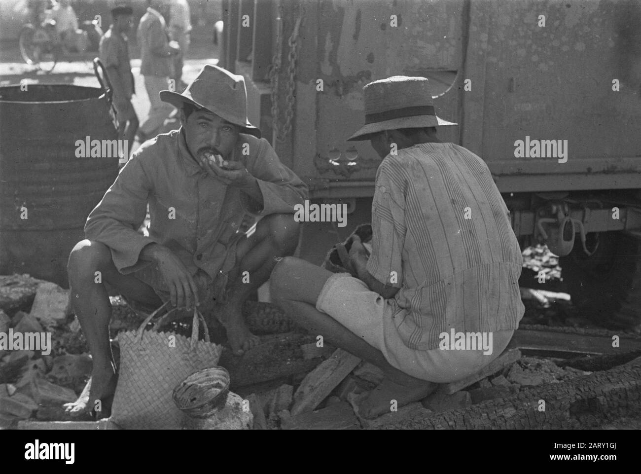 Photo report Palembangs Due uomini indonesiani con cesti mangiare qualcosa in mezzo detriti Data: 1947 luogo: Indonesia, Indie orientali olandesi Foto Stock