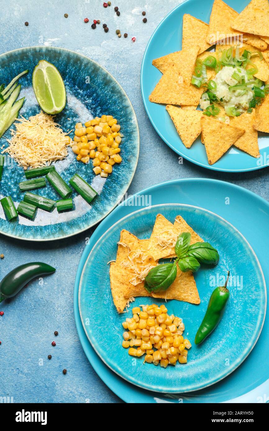 Piatti con gustosi nachos, mais e formaggio su sfondo colorato Foto Stock