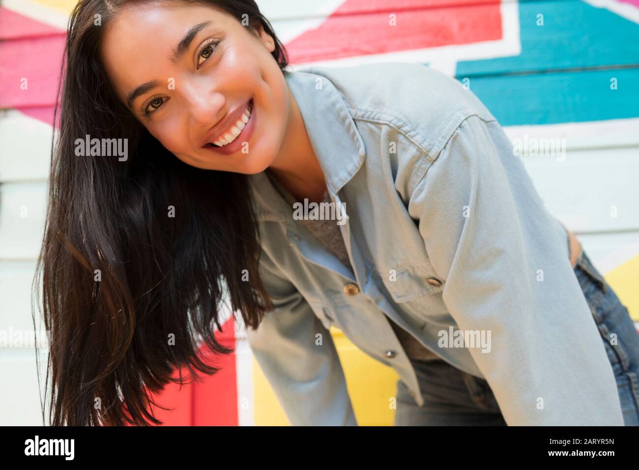 Donna sorridente appoggiata in avanti contro una parete colorata Foto Stock