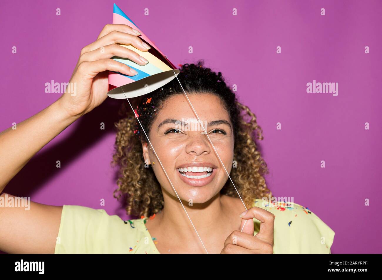 Donna sorridente che mette sul cappello della festa Foto Stock