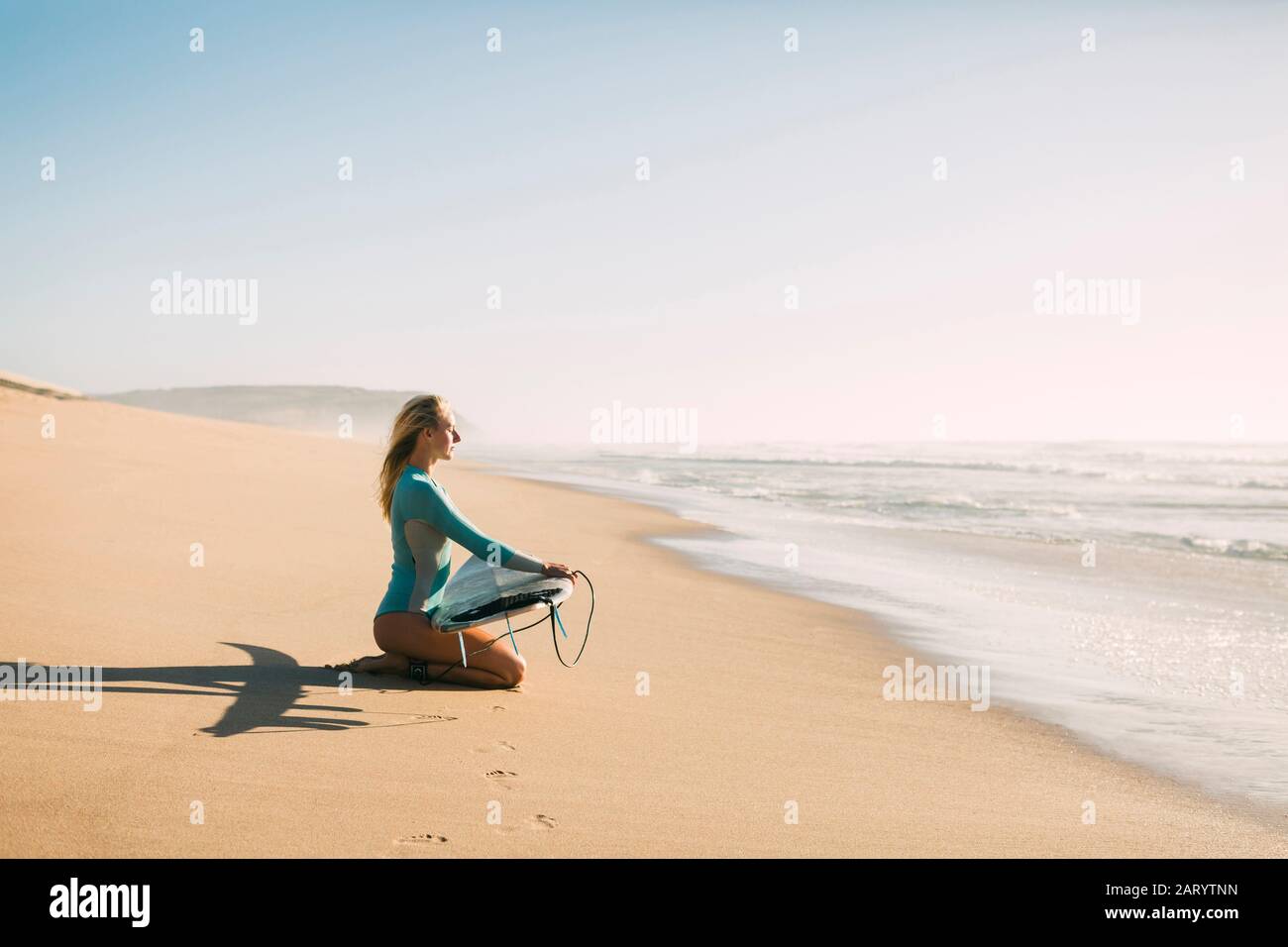 Donna inginocchiata tenendo la tavola da surf sulla spiaggia Foto Stock