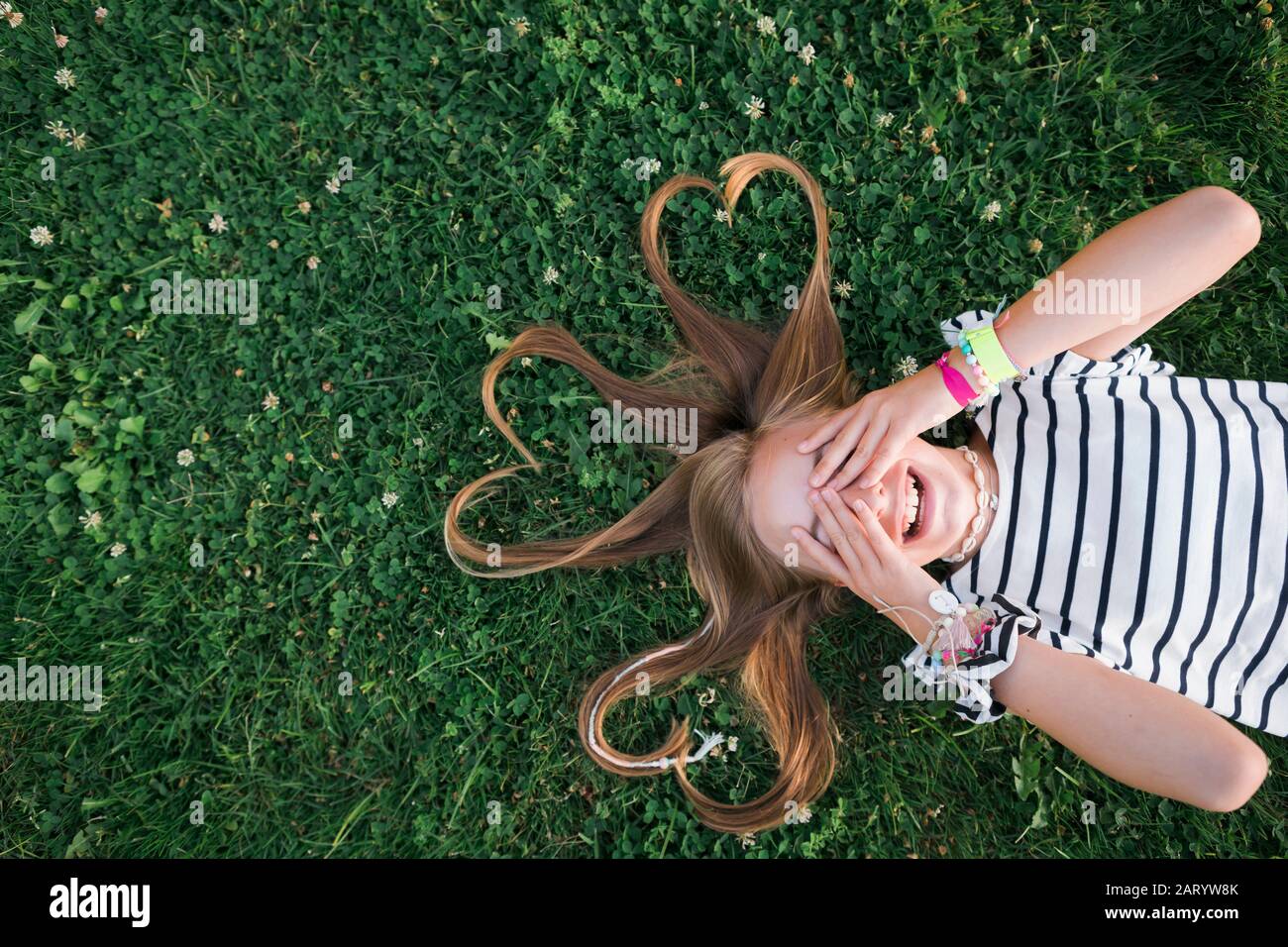 Ragazza con i suoi capelli in forme del cuore che giace sull'erba Foto Stock
