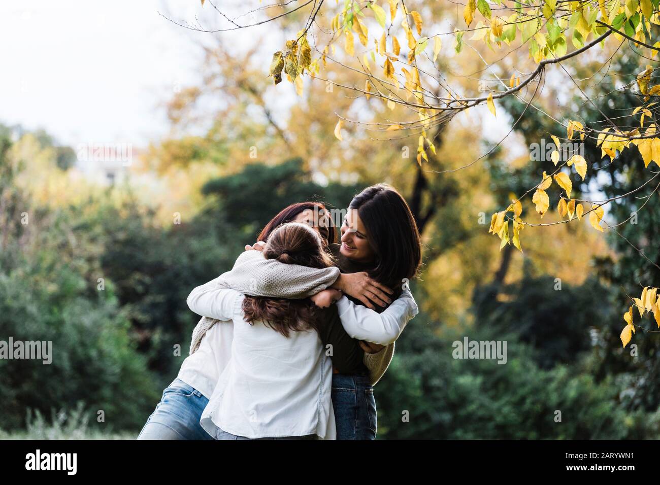 Madre e figlie sorridenti e abbracciati da alberi Foto Stock