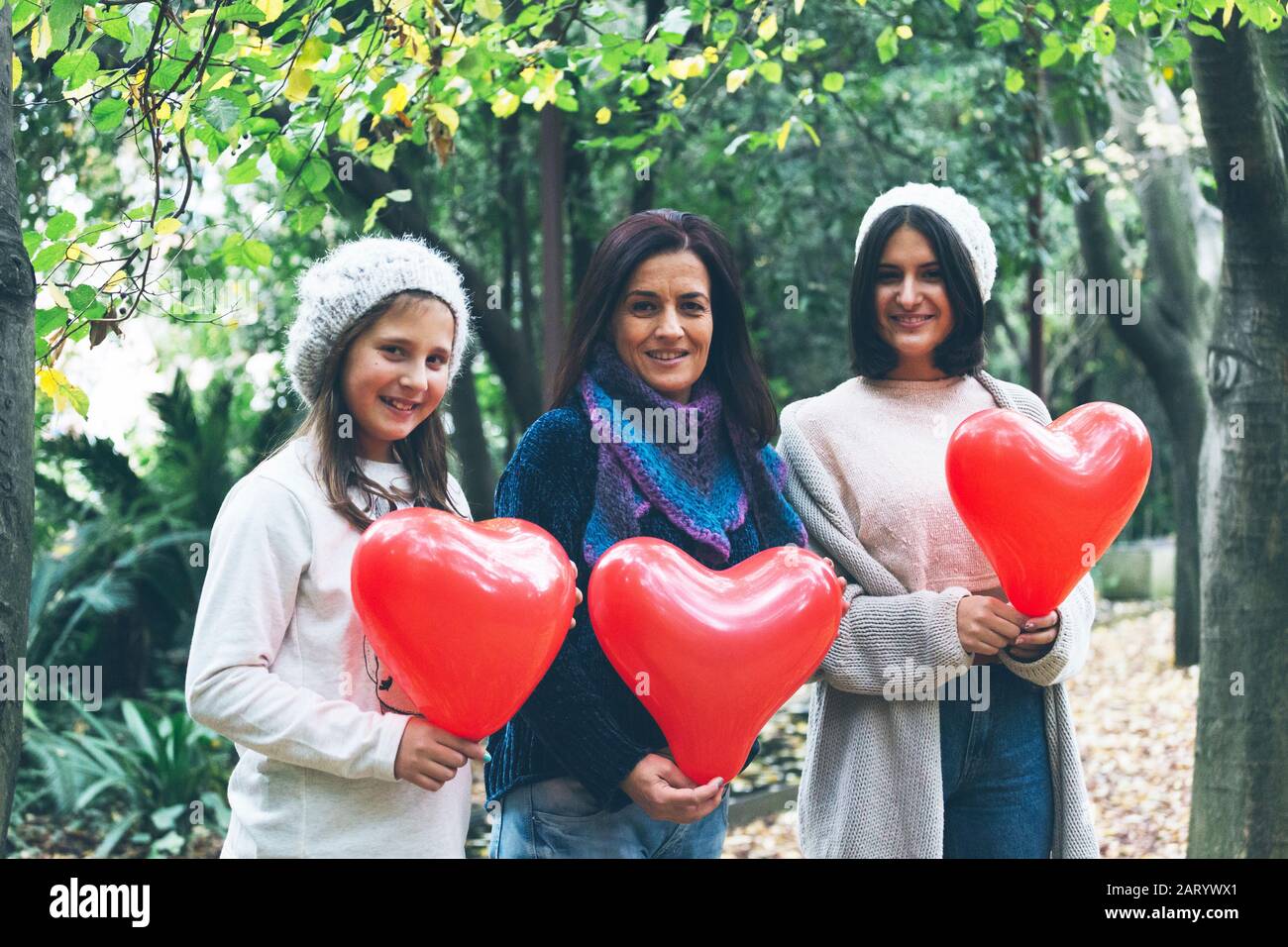 Madre e figlie che tengono palloncini cuore da alberi Foto Stock