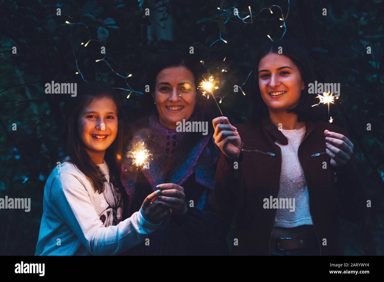 Madre e figlie sorridono e tengono sparklers Foto Stock