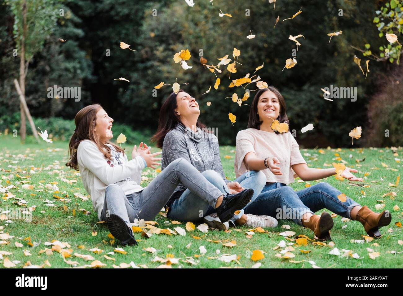 Madre e figlie che giocano in foglie autunnali Foto Stock