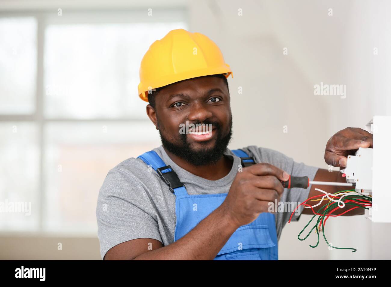 Elettricista afro-americano che esegue il cablaggio in camera Foto Stock