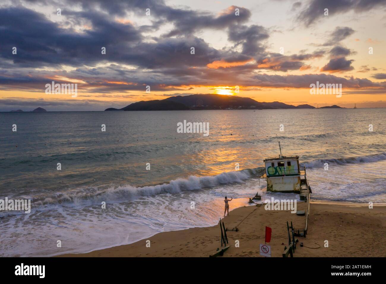 Nha Trang, Vietnam alba con sud Cina Mare, East Sea, isole distanti e un naufragio nave sulla spiaggia in primo piano. La gente sta esercitando Foto Stock