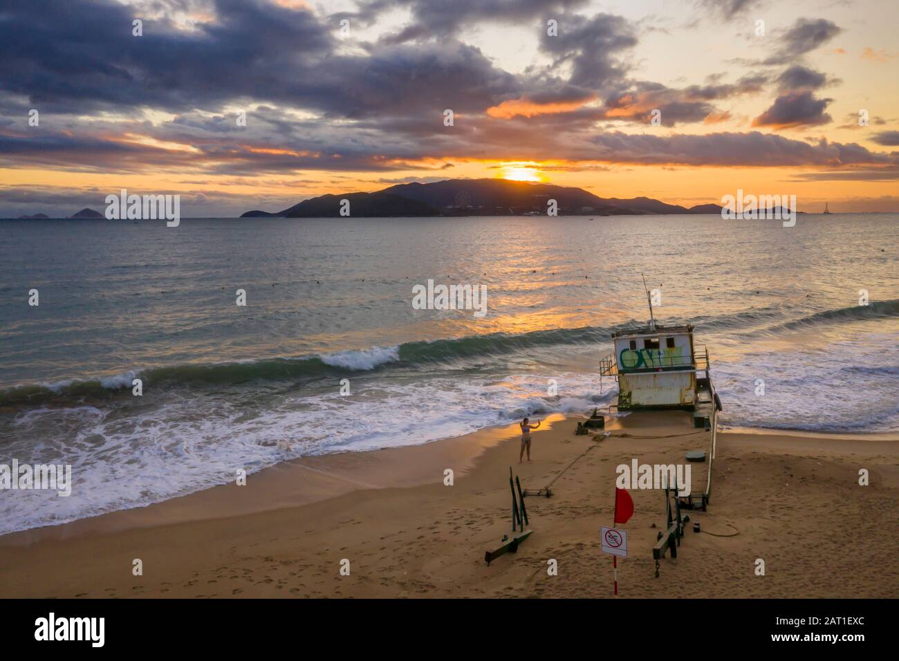 Nha Trang, Vietnam alba con sud Cina Mare, East Sea, isole distanti e un naufragio nave sulla spiaggia in primo piano. La gente sta esercitando Foto Stock