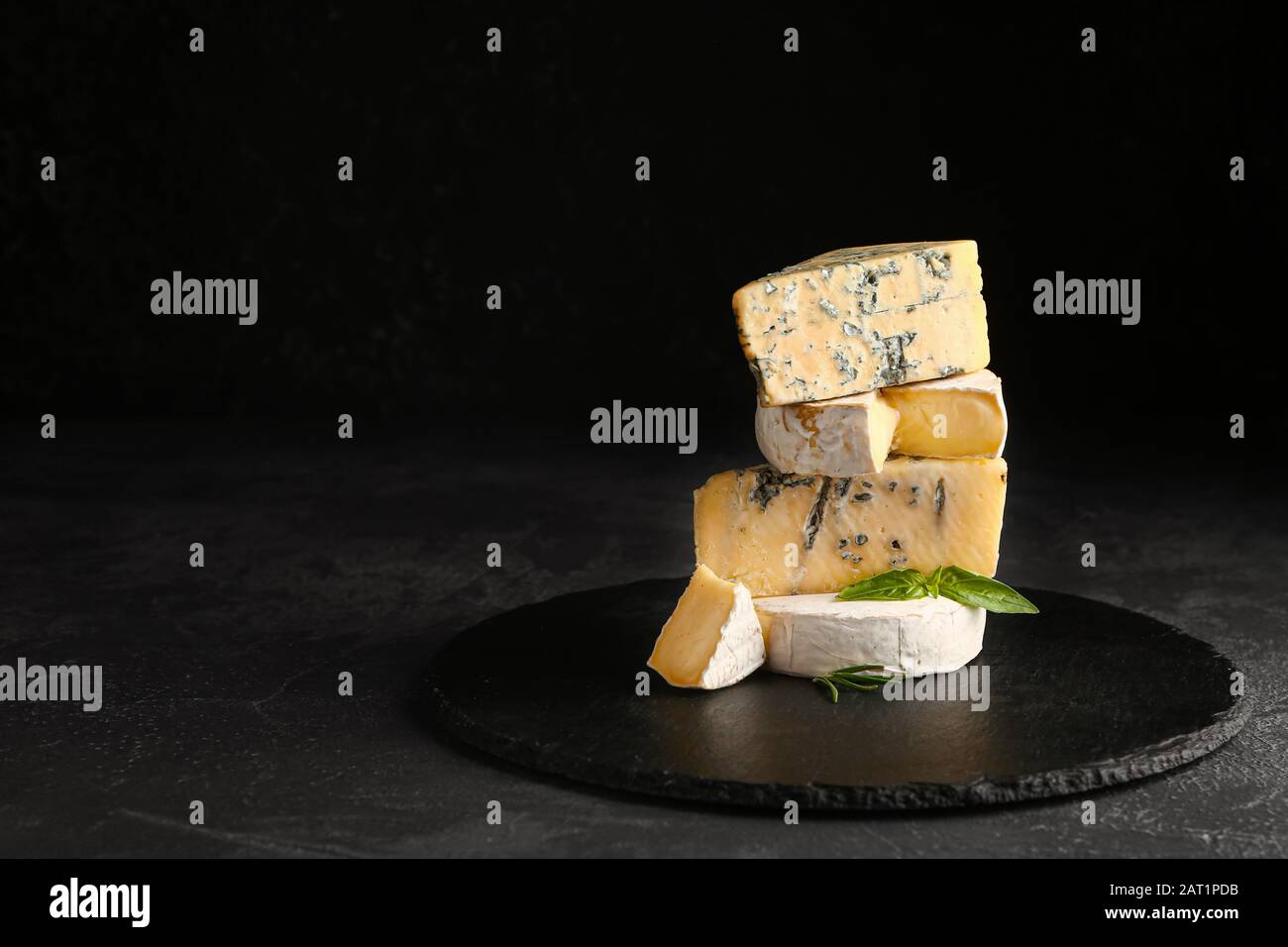 Piatto di ardesia con formaggi freschi su fondo scuro Foto Stock