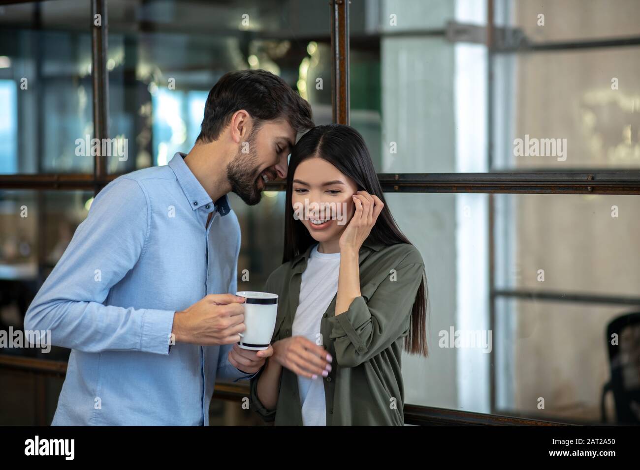 Giovane uomo alto con una tazza di caffè che si flirtare con il suo collega Foto Stock