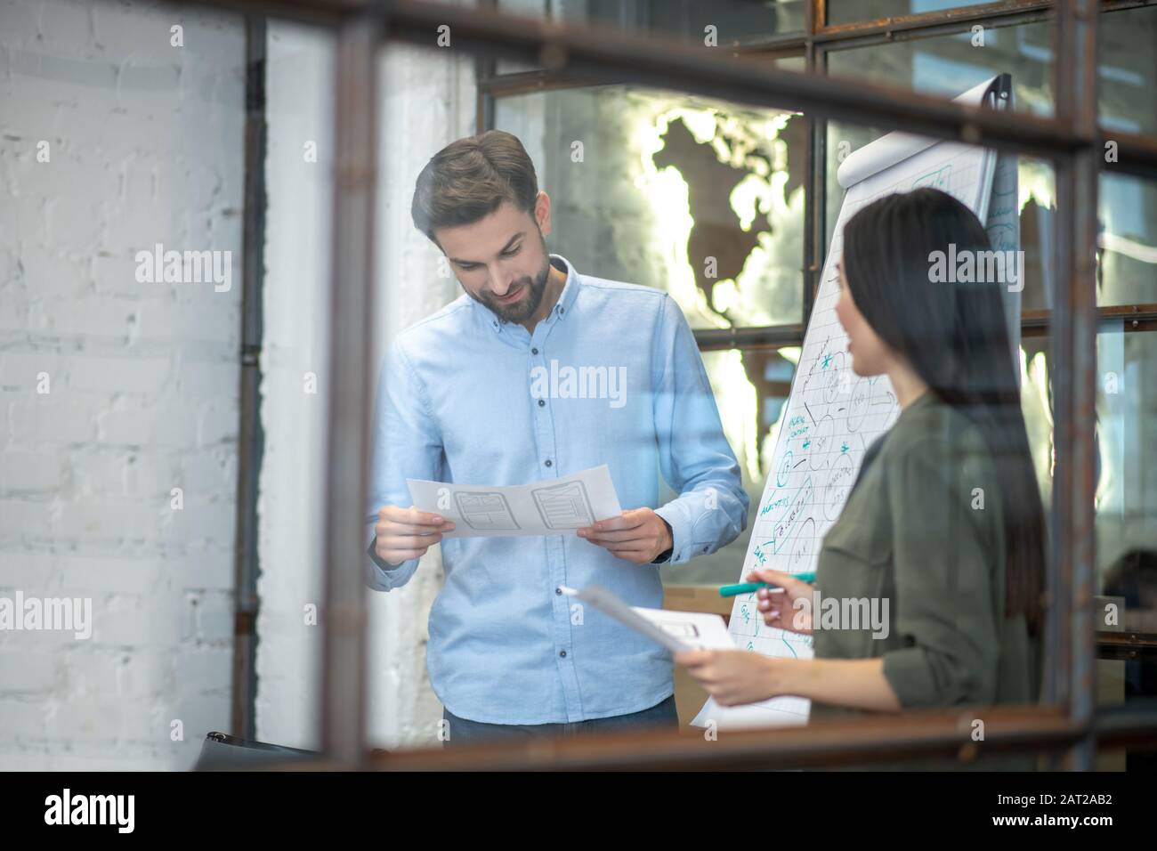 Uomo barbuto in una camicia blu che legge qualcosa in ufficio Foto Stock