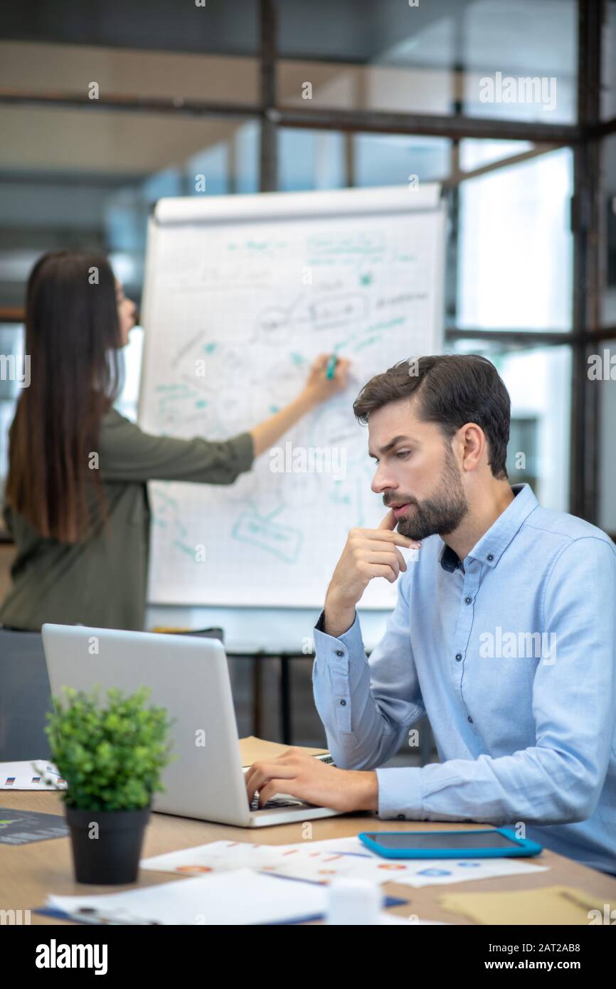 Uomo con bearded in una camicia blu seduto al tavolo e lavorando sul laptop Foto Stock