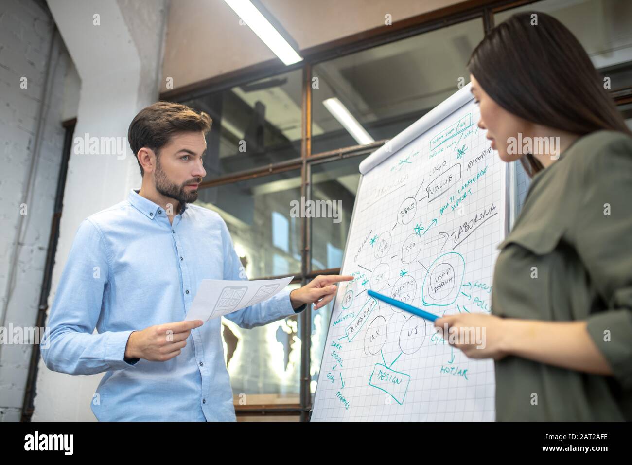 Uomo con bearded in una camicia blu che punta allo sketh sulla lavagna a fogli mobili Foto Stock