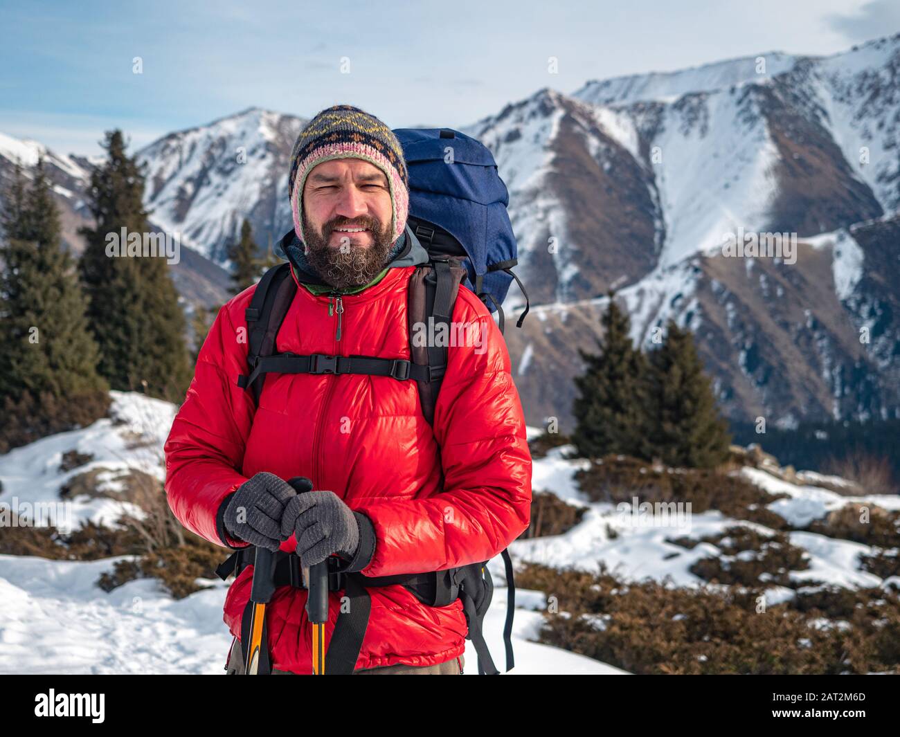 Turista barbuto in inverno. Un uomo con uno zaino e una calda giacca cremisi Foto Stock