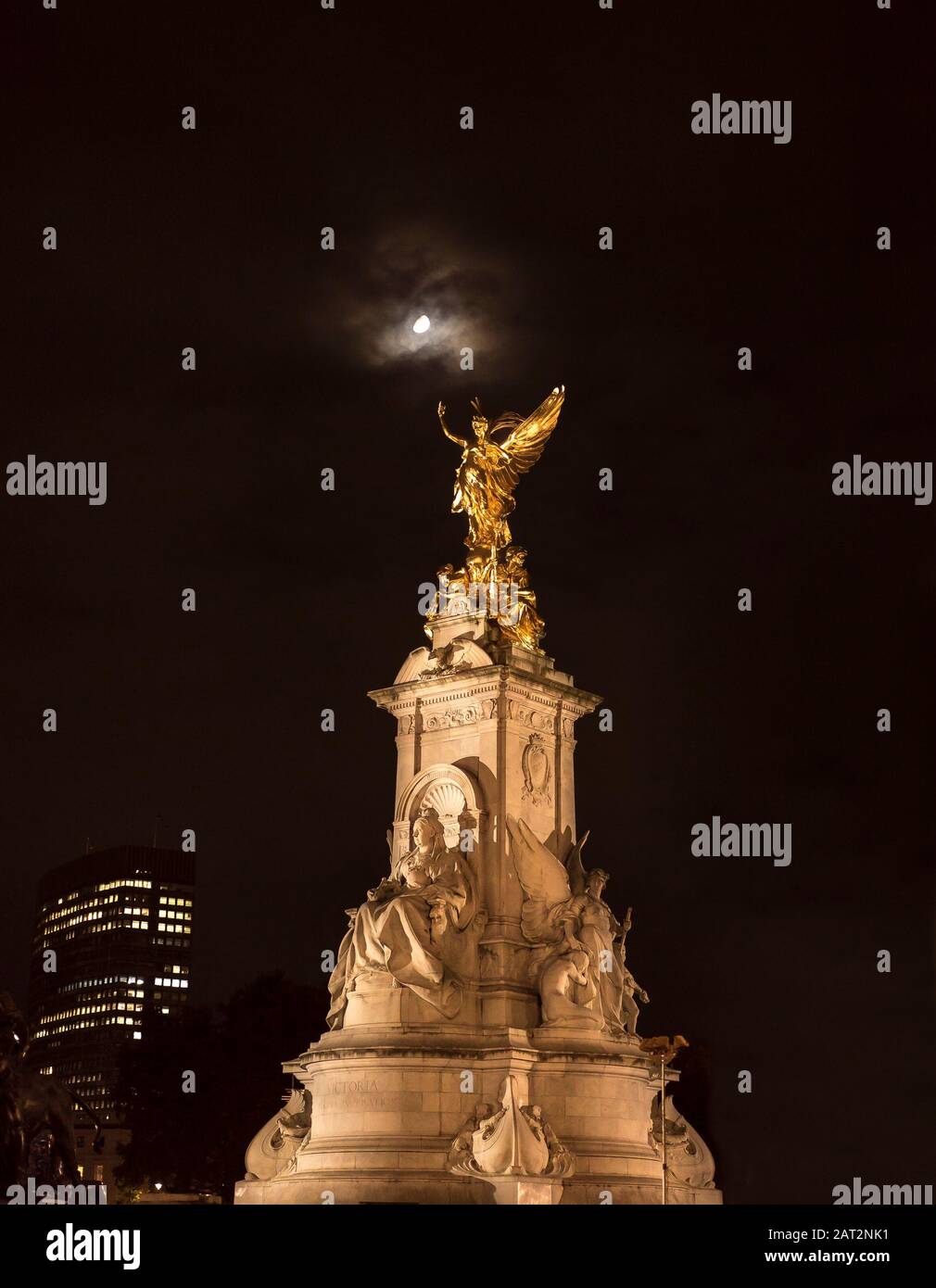 Vista notturna ad angolo basso, la statua commemorativa della Regina Vittoria di Buckingham Palace illuminata, isolata in cielo scuro; la statua della Vittoria alata splende di luce lunare. Foto Stock