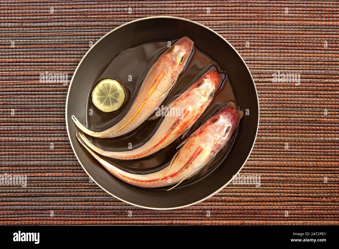 Il pesce fresco isolato viene pulito e preparato per la cottura con limone e spezie in olio in una padella su fondo naturale Mat. Gurnard recentemente catturato Foto Stock