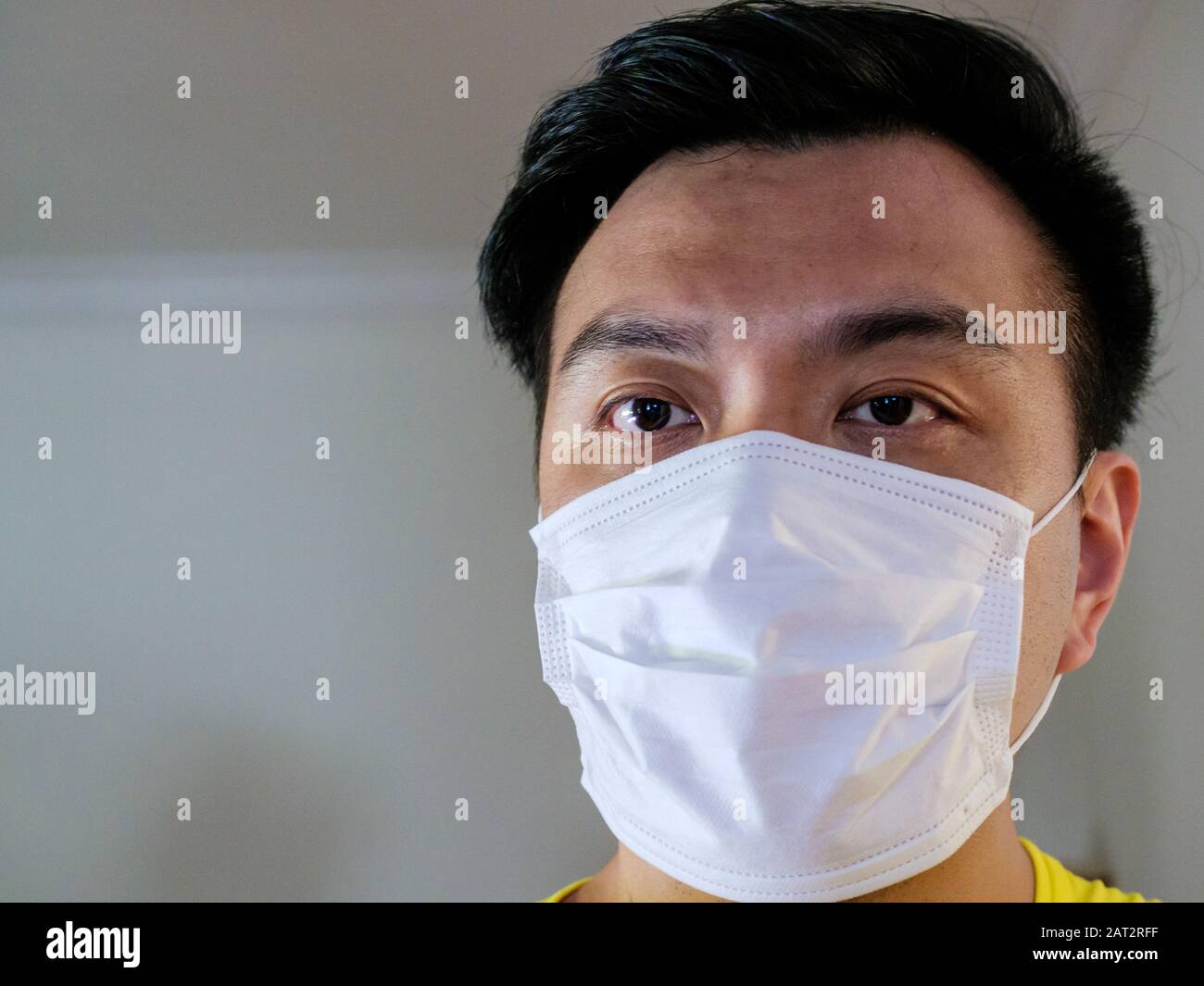 Testa di asiatico cinese uomo / persona con un'espressione preoccupata indossando una maschera chirurgica viso come protezione contro la trasmissione / infezione di contag Foto Stock