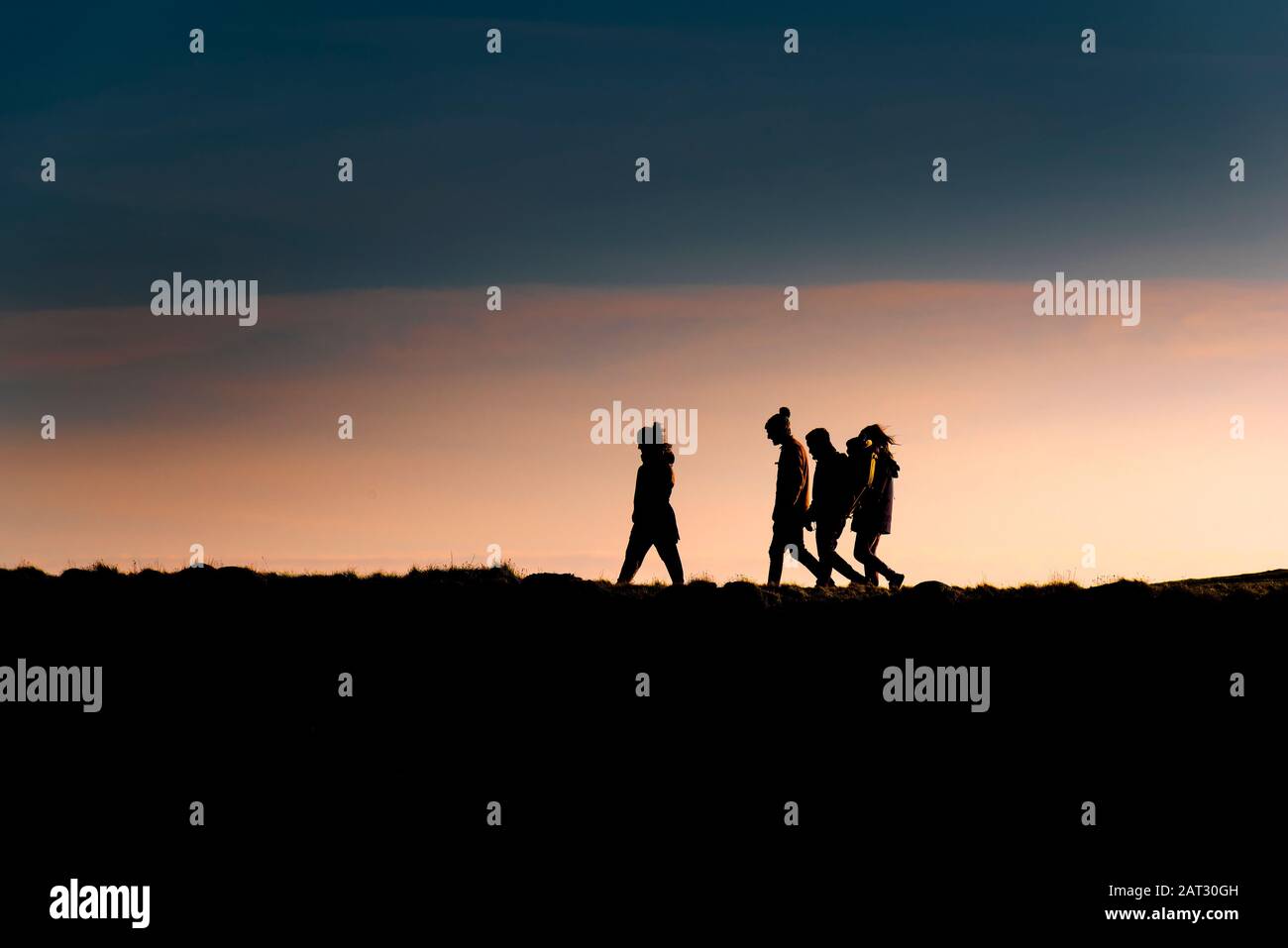 Un gruppo di amici che camminano a casa mentre il sole tramonta alla fine della giornata. Foto Stock