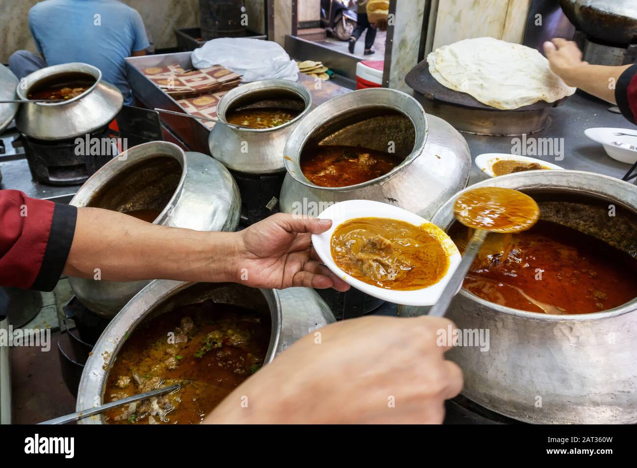 Un operaio del ristorante che spooning un curry di monton dal vaso grande ad uno del ristorante a Chandni Chowk in India vecchia Delhi Foto Stock