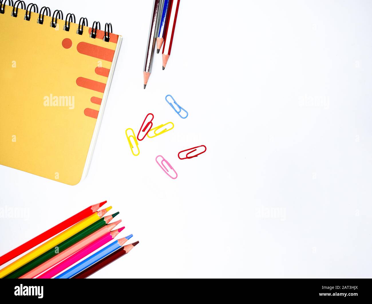 Materiali di studio sparsi su una tabella bianca, che contiene un taccuino, tre matite, sei pastelli e alcune graffette. Foto Stock