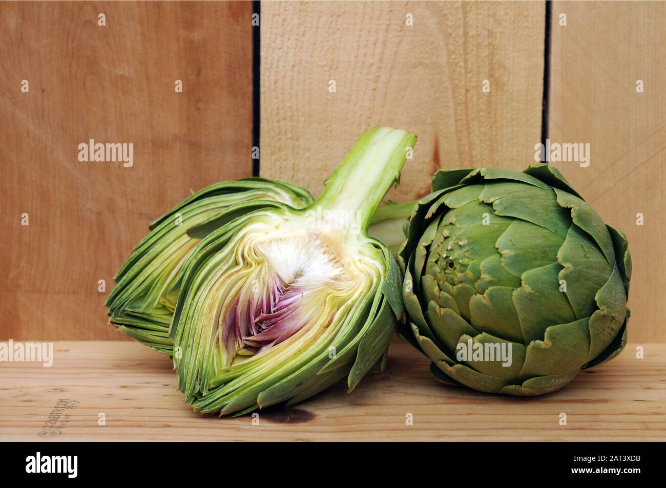 Closeup intero e tritato carciofo fresco su tavola di legno Foto Stock