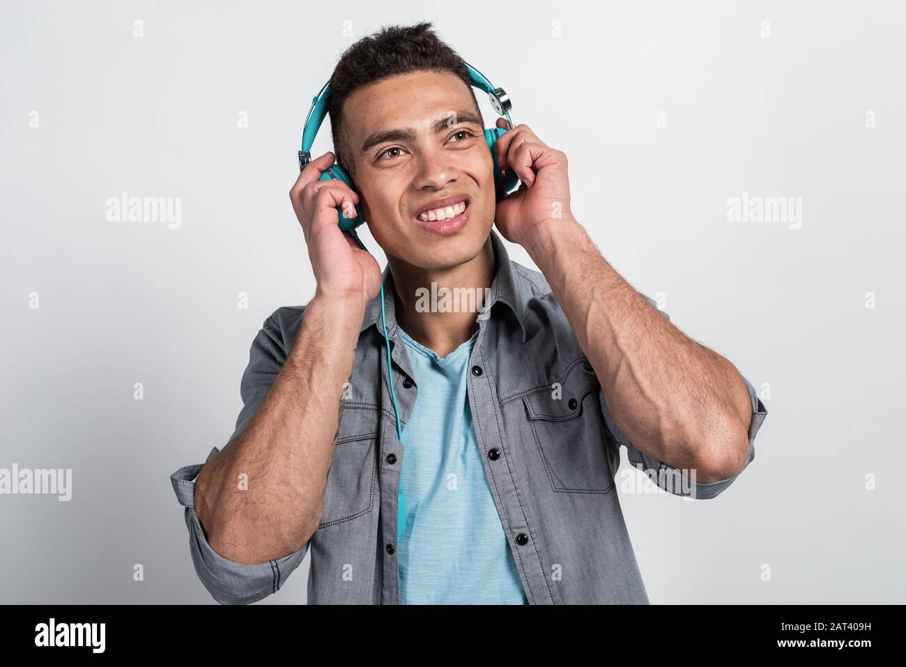 Giovane uomo felice con piacere ascolta musica e gli occhi in su, tocca gli auricolari con le mani Foto Stock