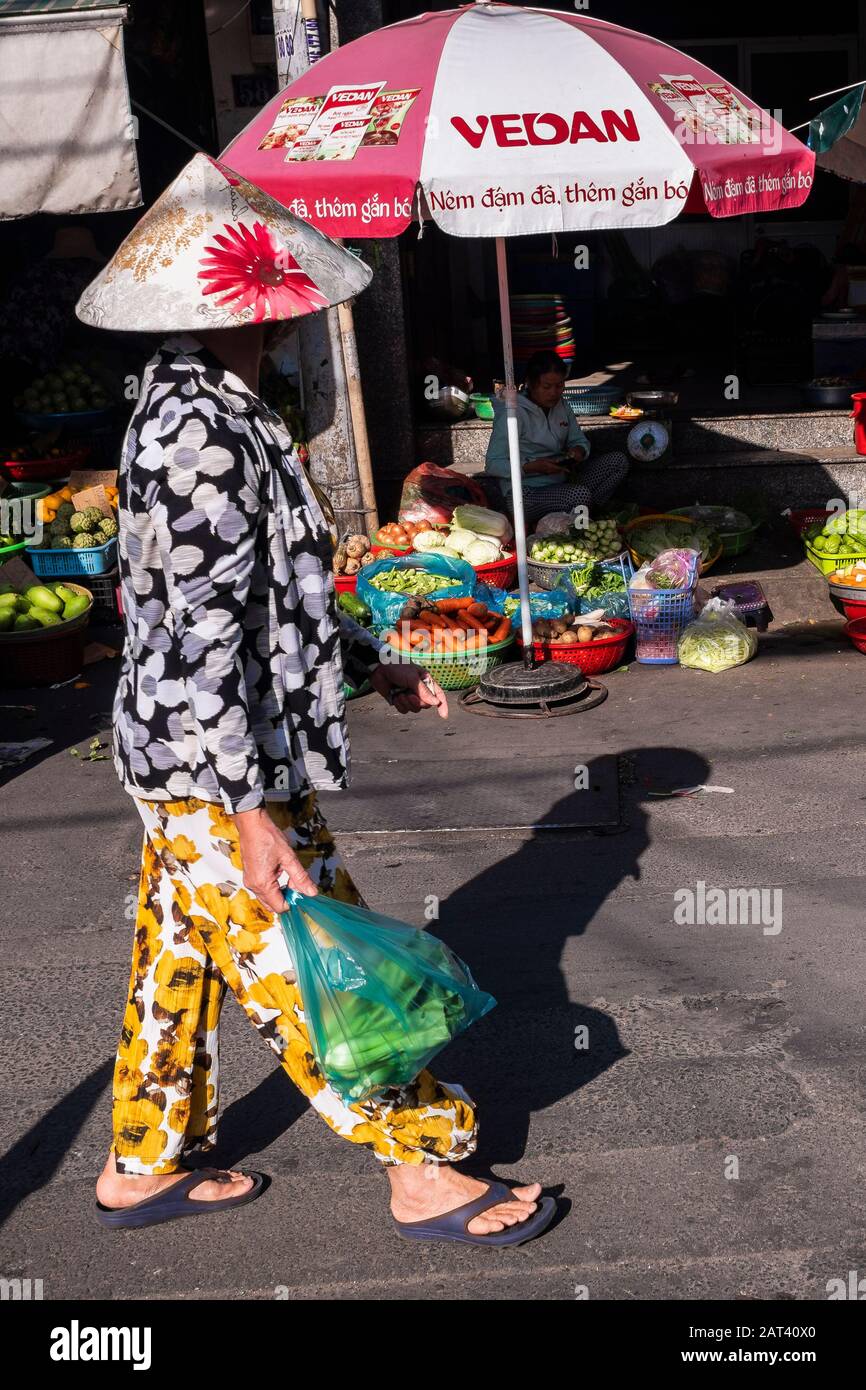 Donna che porta lo shopping in borse di plastica a piedi attraverso il mercato di strada, ho Chi Minh City, Vietnam Foto Stock