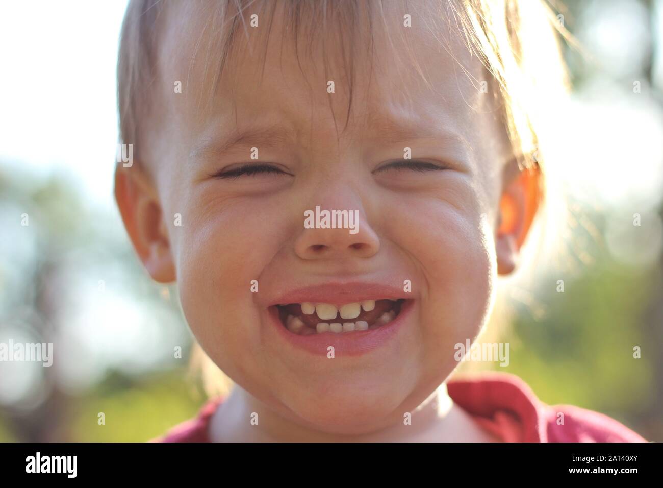 Pianto bambino bianco con denti bianchi e sfondo estivo sfocato. Foto Stock