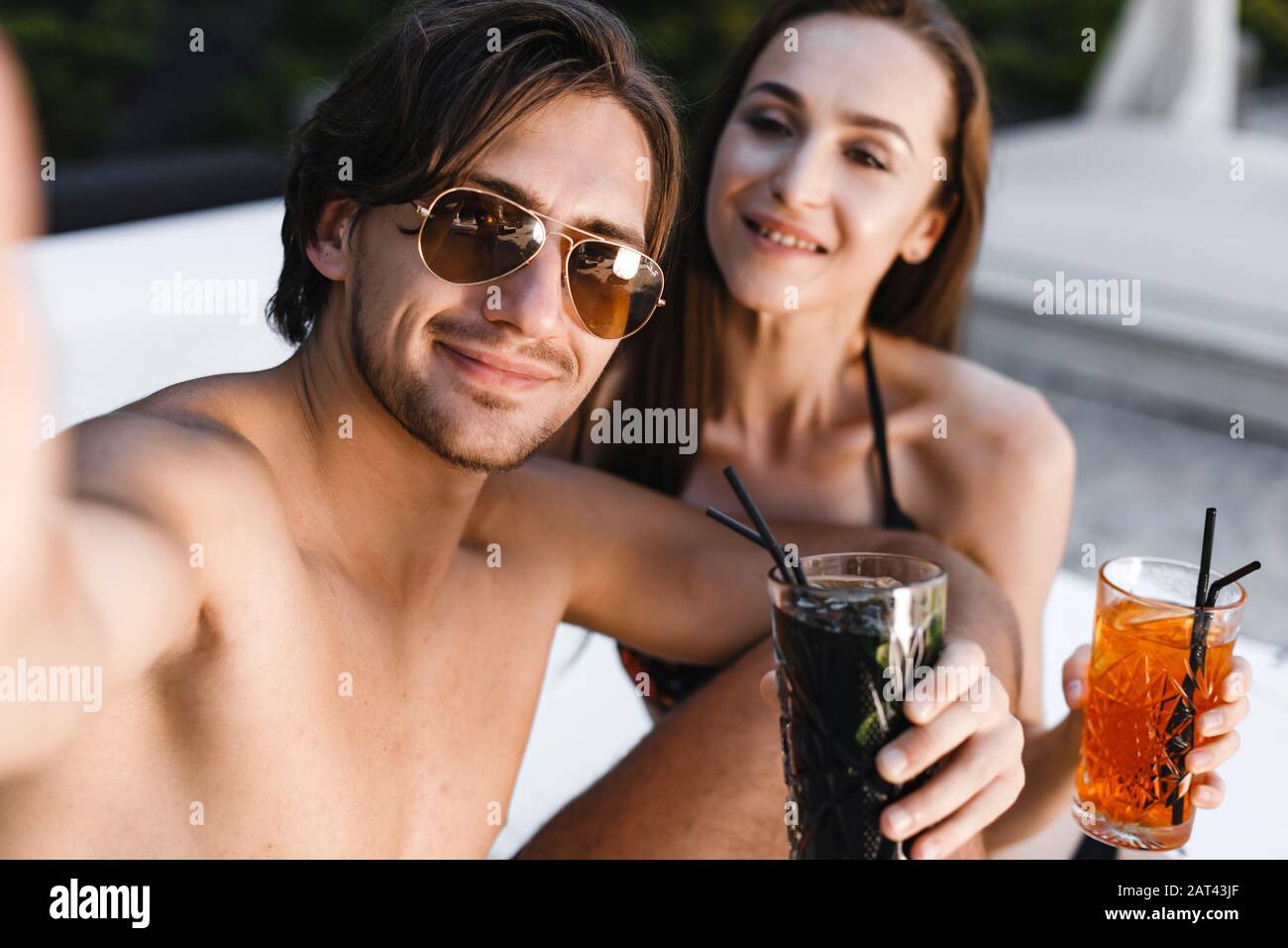 Coppia sorridente che fa selfie e tiene cocktail in spiaggia Foto Stock