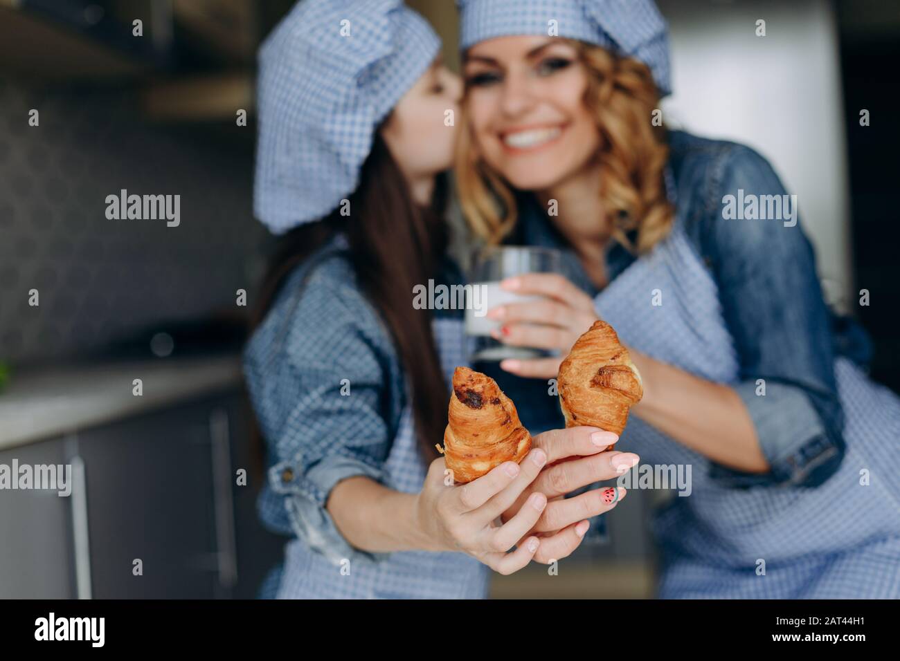 Ragazza che bacia sua madre. Tengono un croissant e lo mostrano a mano dritta Foto Stock