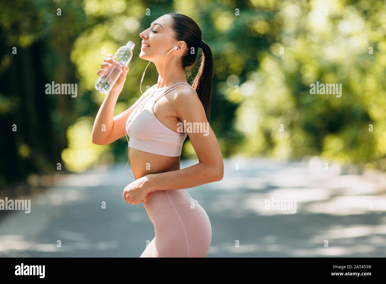Ragazza sportiva in cuffie bevande acqua in piedi nel parco all'aperto .- immagine Foto Stock