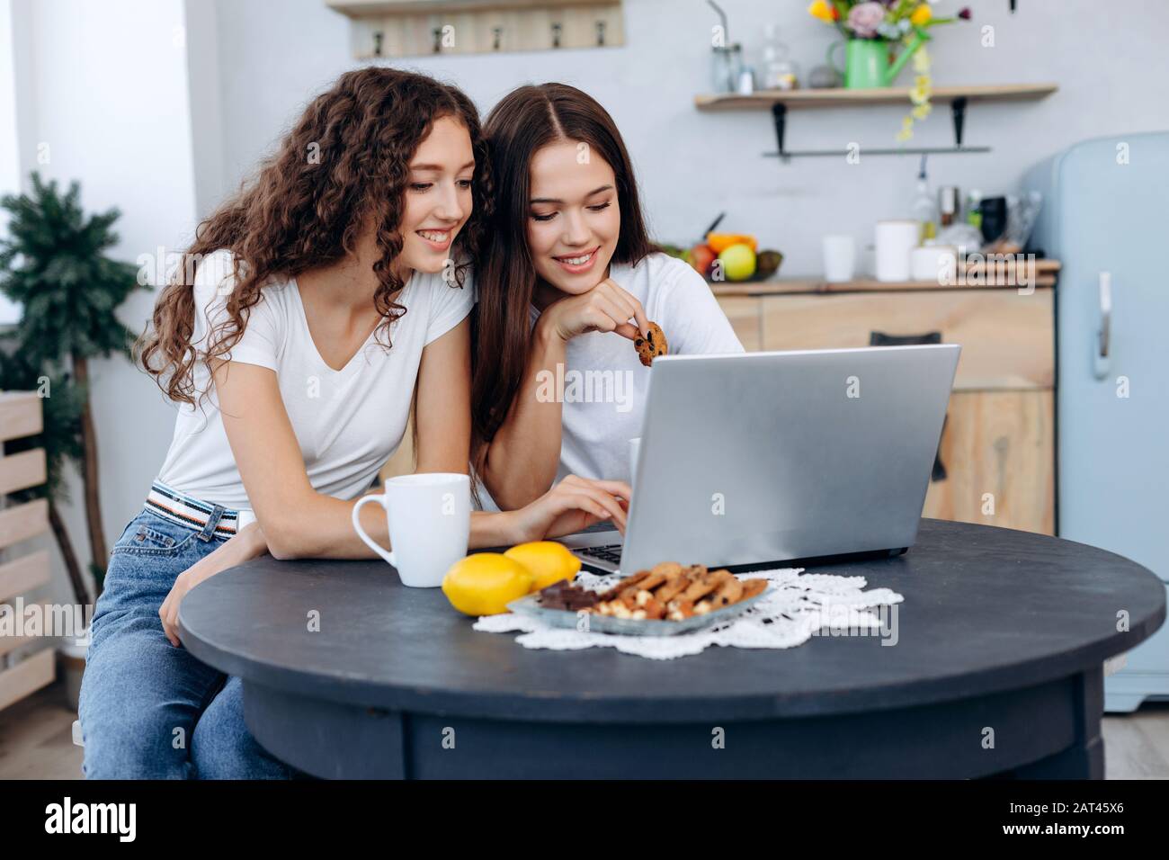 Ragazze attraenti che bevono tè e che guardano qualcosa sul Internet al tavolo da cucina. Foto Stock