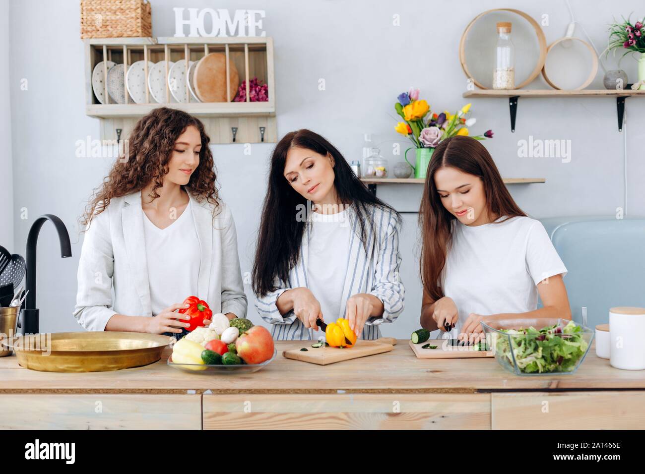 Madre felice e le sue figlie carine affettare le verdure in cucina. Foto Stock