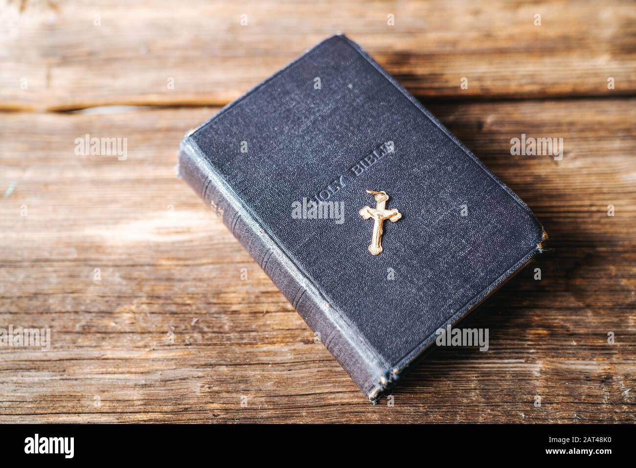 Vecchia Bibbia dura coperta e crocefisso dorato su uno sfondo di legno Foto Stock