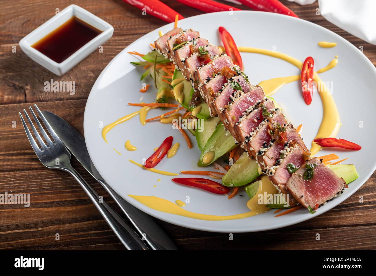 Cucina giapponese. Tataki con tonno. Pesce fritto con semi di sesamo e salsa di soia, wasabi, lime. Su un cuscino di verdure. Avocado, strisce di peperoncino Foto Stock