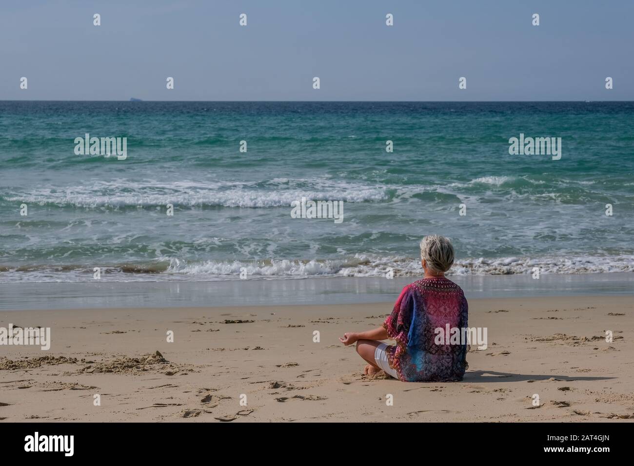 Donna anziana con capelli grigi e un abito bianco rilassante sulla spiaggia medita i capelli sulla spiaggia Foto Stock