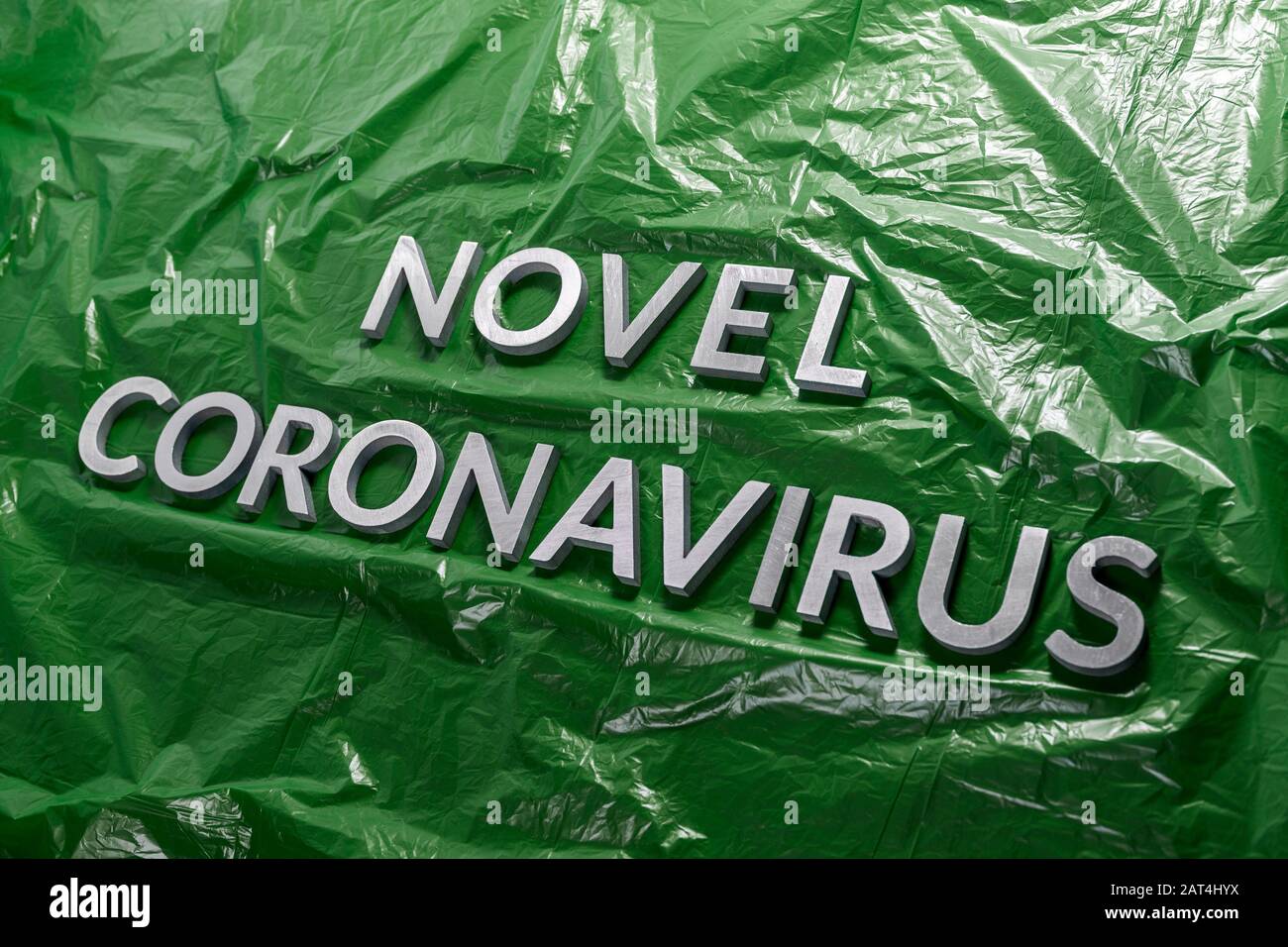 Le parole novello coronavirus posato con lettere di metallo d'argento su pellicola di plastica crumpled verde - composizione diagonale Foto Stock