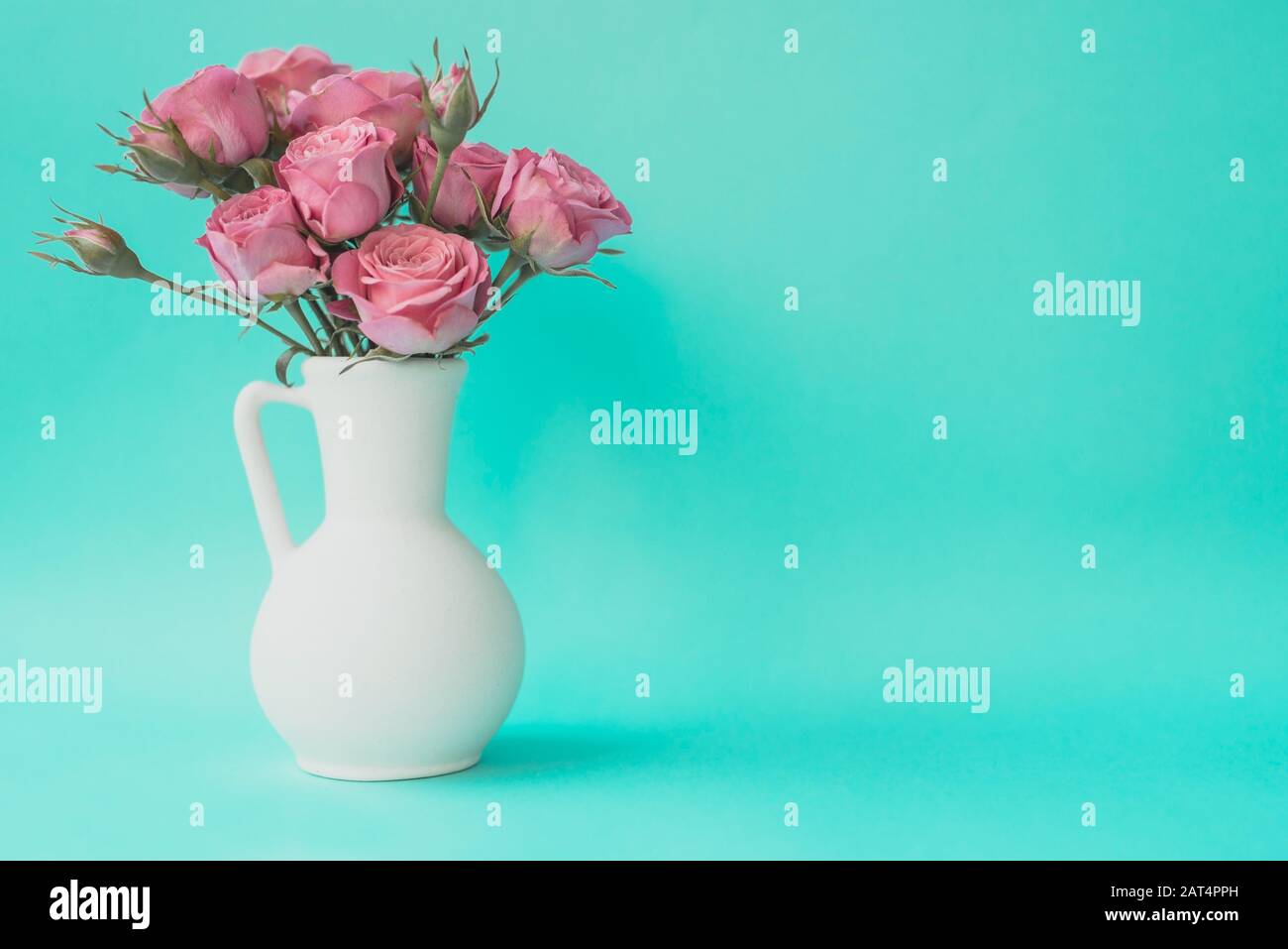 Bouquet di rose rosa in vaso su sfondo turchese. Spazio di copia. Foto Stock