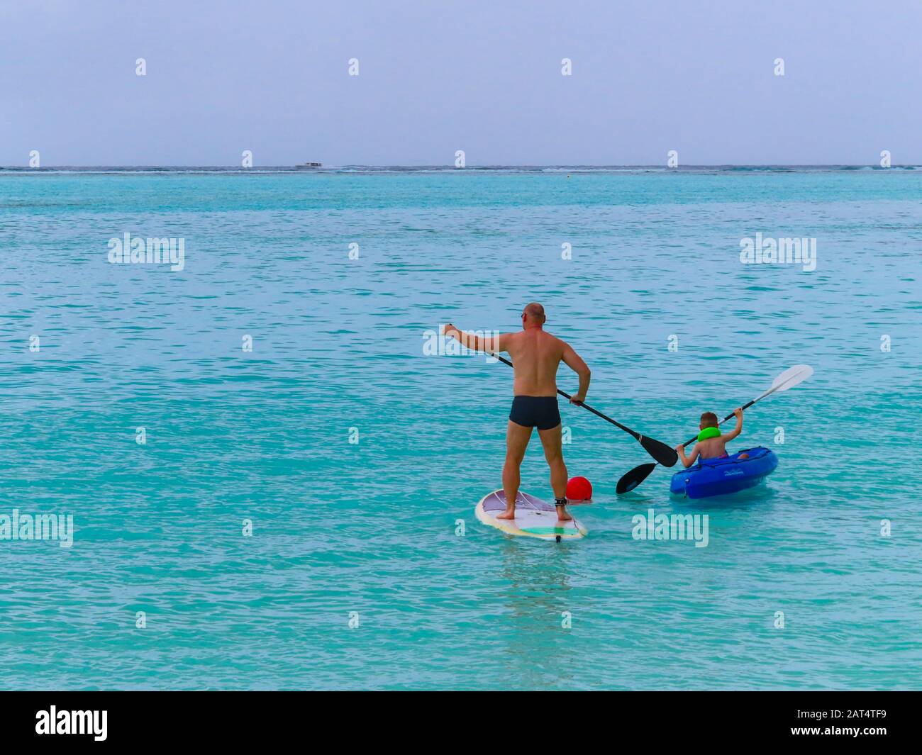 Padre e Figlio godendo dello sport acquatico alle Maldive. Il paddleboarding del padre e il capretto è kayak fuori di un'isola nell'Atollo di Ari del sud Foto Stock