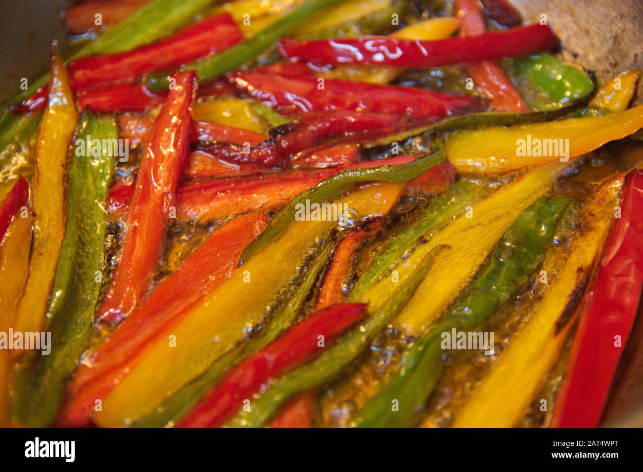 Primo piano di una teglia in cui i peperoni tagliati a strisce vengono fritti, sono peperoni rossi, verdi e gialli in abbondante olio caldo Foto Stock
