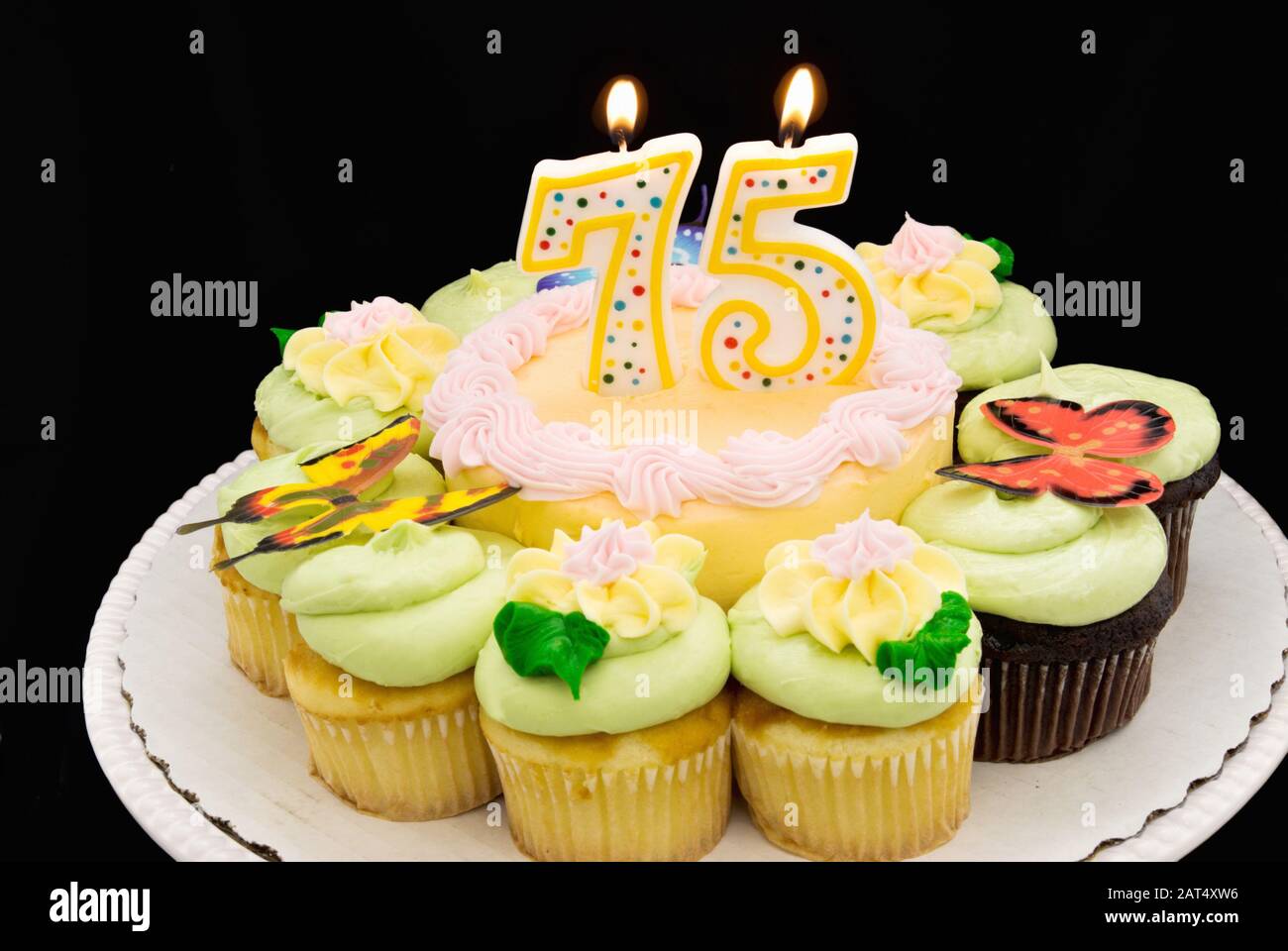 Torta di compleanno con crema di burro color pastello circondata da cupcake. Un numero 75 settantacinque candela sta bruciando nel mezzo della torta. Foto Stock