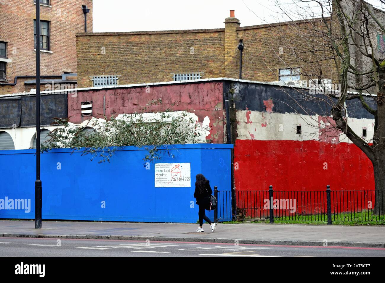 Una figura femminile solitaria che cammina attraverso i colorati hardings dei locali chiusi del negozio nella strada commerciale Limehouse East London England UK Foto Stock