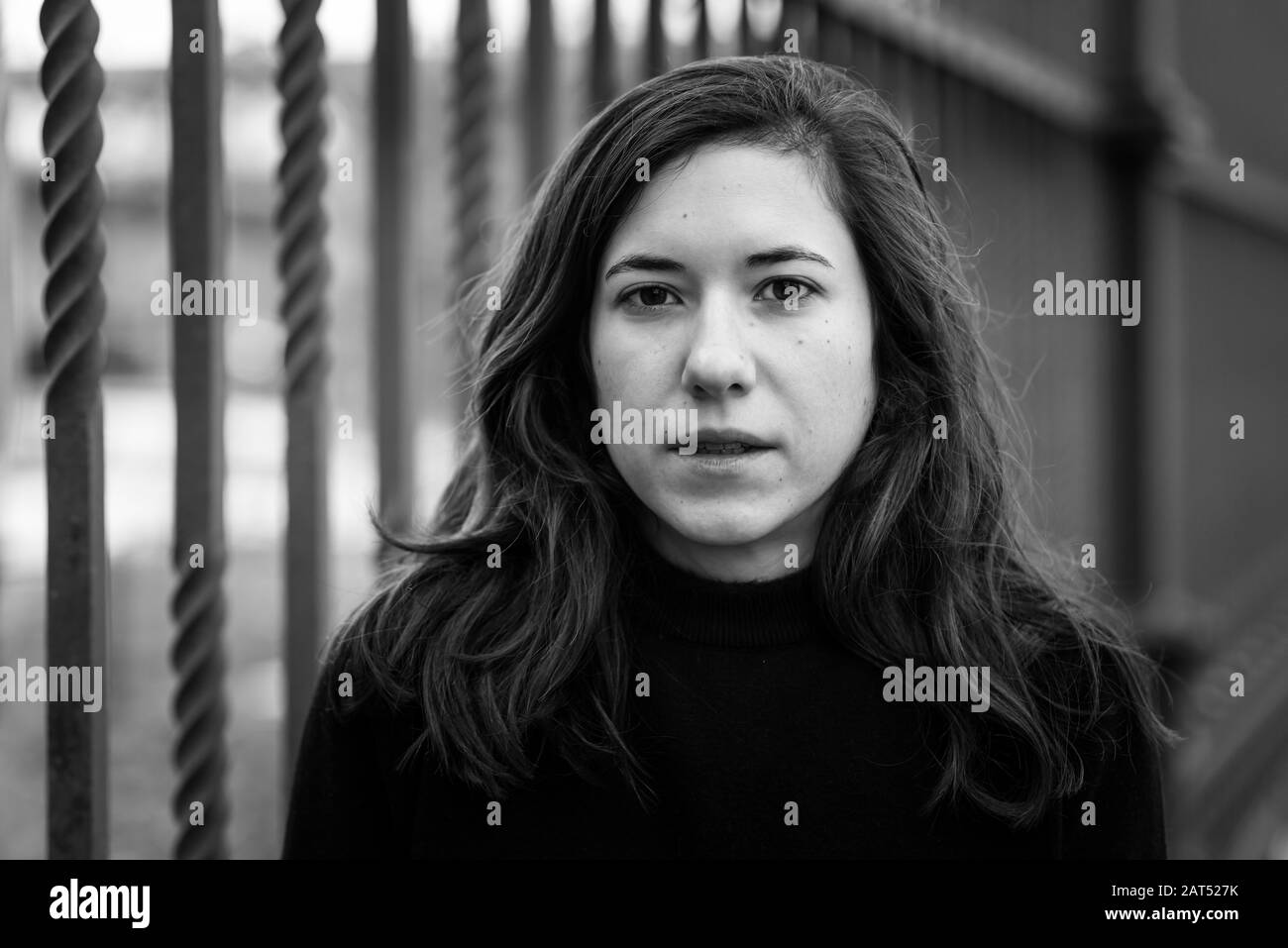 Attraente giovane donna bianca con capelli castani che posano contro una recinzione metallica Foto Stock