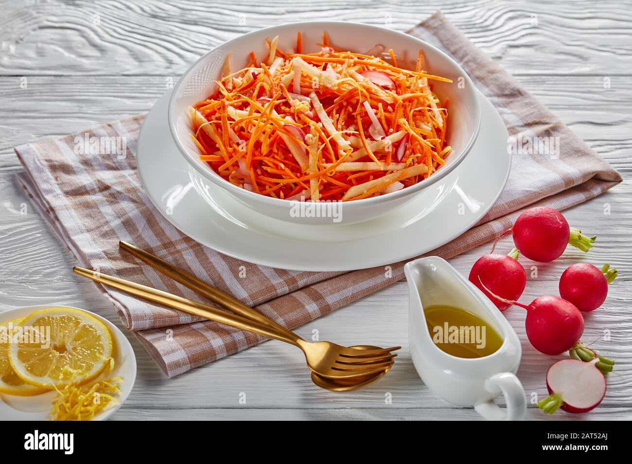 poche calorie di ravanello di carota e insalata di mele cosparse di semi di quinoa e scorza di limone in una ciotola bianca con una forchetta d'oro e cucchiaio su un tavolo di legno, Foto Stock