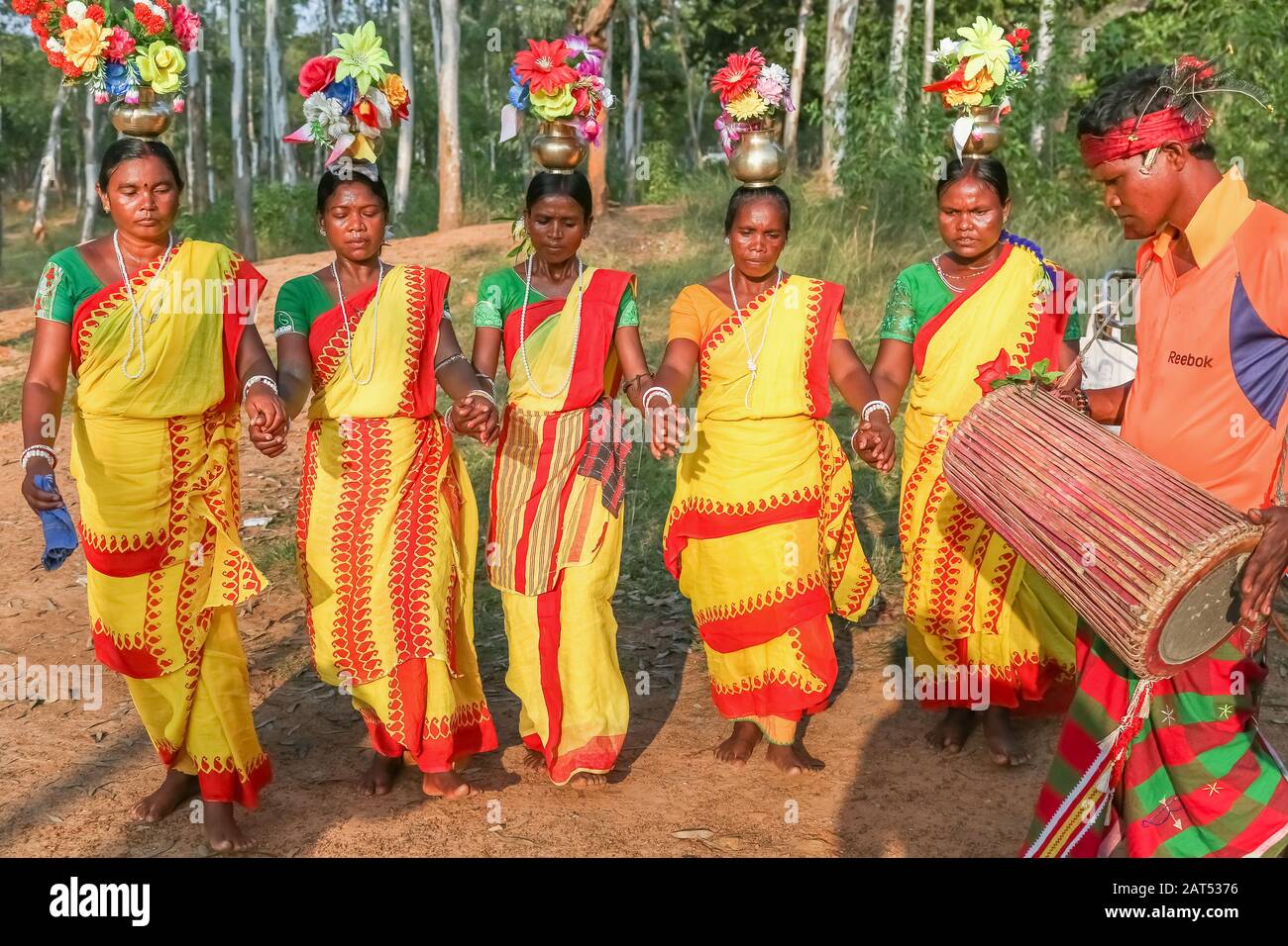 L'uomo tribale suona uno strumento musicale mentre le donne eseguono la danza popolare in un'area boschiva a Bolpur Shantiniketan, Bengala Occidentale Foto Stock